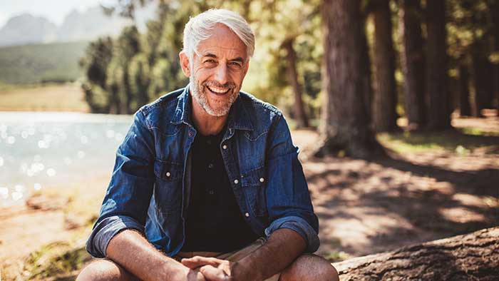 Mature man sitting near a lake looking at camera and smiling.