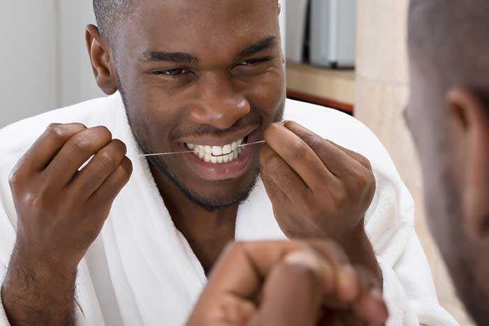 Young man flossing his teeth in front of mirror